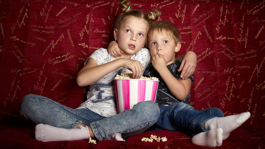 Junge und Mädchen mit Popcorn auf einem Sofa, sichtlich erschrocken über das Filmgeschehen.