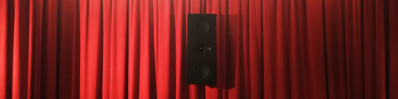 Ein einzelner Lautsprecher als Surround Back Center für 6.1 vor einem roten Vorhang.