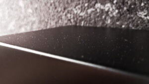 Gut sichtbarer Staub auf der matt-schwarzen Oberfläche eines Lautsprechers.